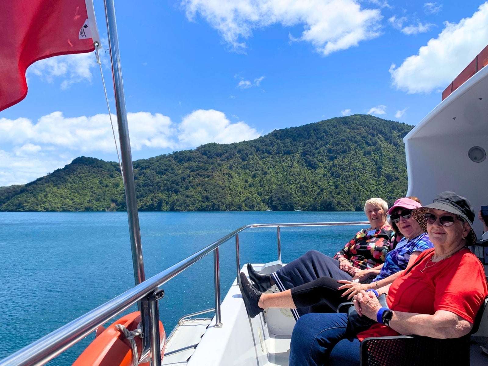 Guests sitting on boat deck with Queen Charlotte Sound in background